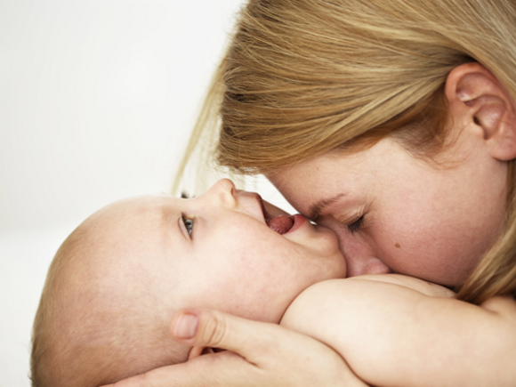 Majka daje poljubac bebi koja se smije za vrijeme masaže bebe