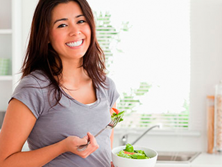 Žena se smije i drži zdjelu salate i vilicu u ruci