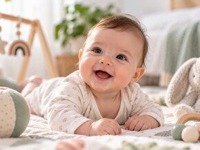 Beba od 4 meseca leži na leđima i pruža ruku prema igrački