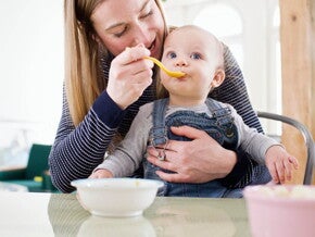 Majka za stolom hrani svoju bebu Majka za stolom hrani svoju bebu