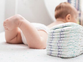 Photograph: baby lying on a bed next to a stack of diapers