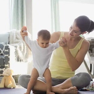 Majka pomaže bebi pri prvim koracima u dnevnoj sobi.