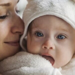 Majka drži bebu blizu lica dok beba gleda u kameru i istražuje okolinu, što predstavlja ranu fazu komunikacije i razvoja govora kod beba.