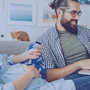 Roditelji sede kod kuće i zajedno planiraju porodični budžet za bebu, razgovarajući o troškovima i finansijama u opuštenom okruženju.