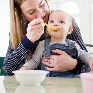 Majka za stolom hrani svoju bebu Majka za stolom hrani svoju bebu