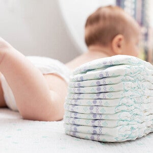 Photograph: baby lying on a bed next to a stack of diapers