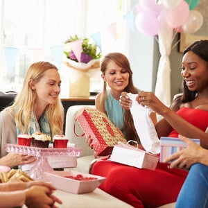 Poklon za trudnice na baby shower proslavi, sa trudnicom koja otvara poklone u društvu prijateljica.