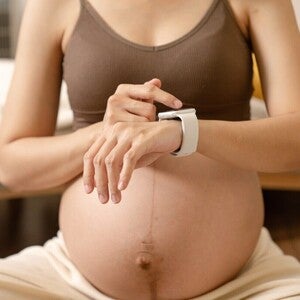 Trudnica sedi, koristi pametni sat na svojoj ruci.