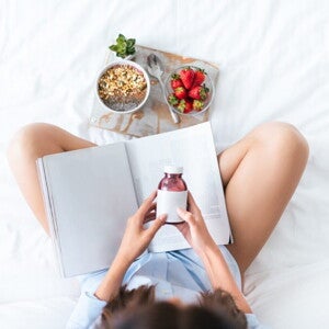 Djevojka na sofi sa knjigom, čita natpis na bočici s vitaminima Djevojka na sofi sa knjigom, čita natpis na bočici s vitaminima