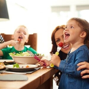 Porodica sedi za stolom, ručaju pizzu i salatu.