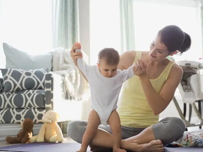 Majka pomaže bebi pri prvim koracima u dnevnoj sobi.