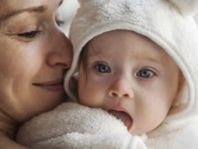 Majka drži bebu blizu lica dok beba gleda u kameru i istražuje okolinu, što predstavlja ranu fazu komunikacije i razvoja govora kod beba.