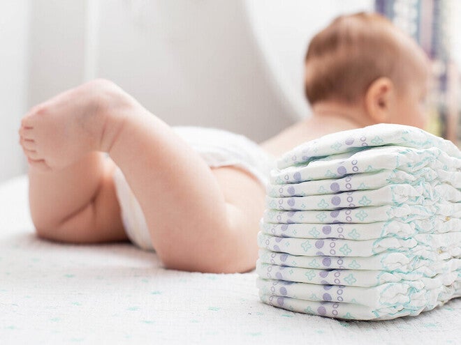 Photograph: baby lying on a bed next to a stack of diapers
