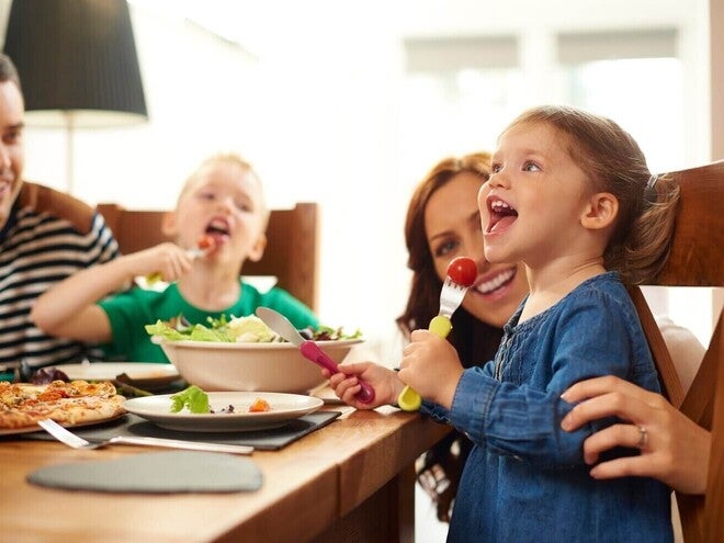 Porodica sedi za stolom, ručaju pizzu i salatu.