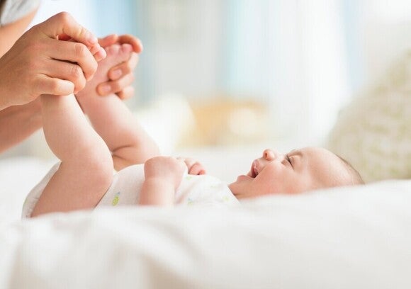 Beba leži na krevetu dok joj odrasla osoba nežno drži stopala tokom igre i interakcije.