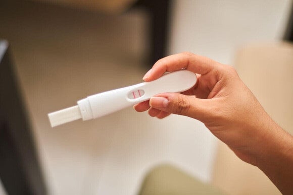 Fotografija ruke koja drži beli test za trudnoću sa ružičastim indikatorom